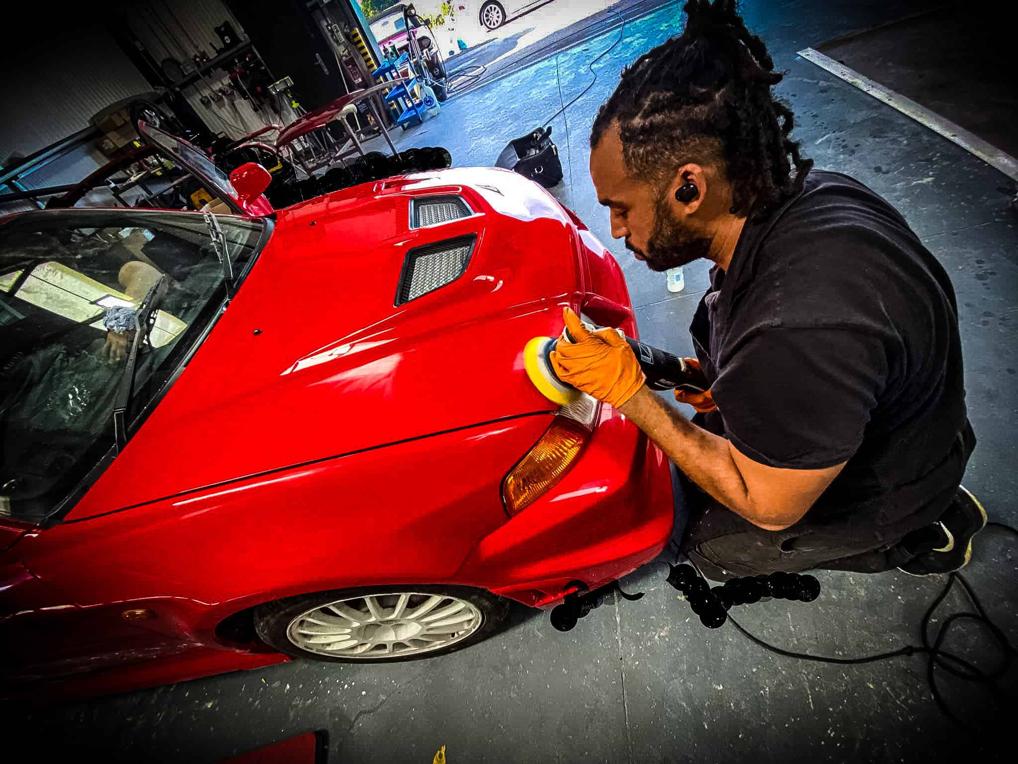A professional detailer polishing a red sports car to restore its shine and flawless finish.